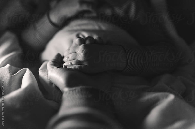 Moody black and white image of a mother holding her child\'s hand at bedtime