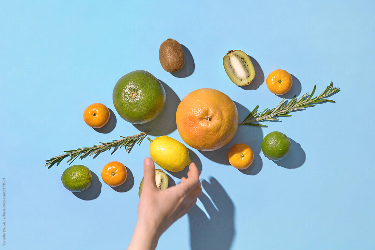 Flat Lay view of tropic citrus fruits on a blue background and a human hand