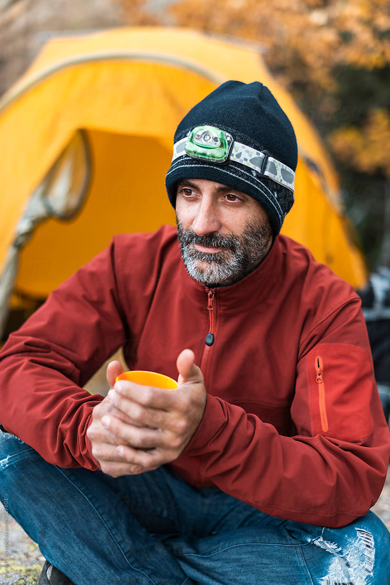 Adult adventurer drinking tea near tent
