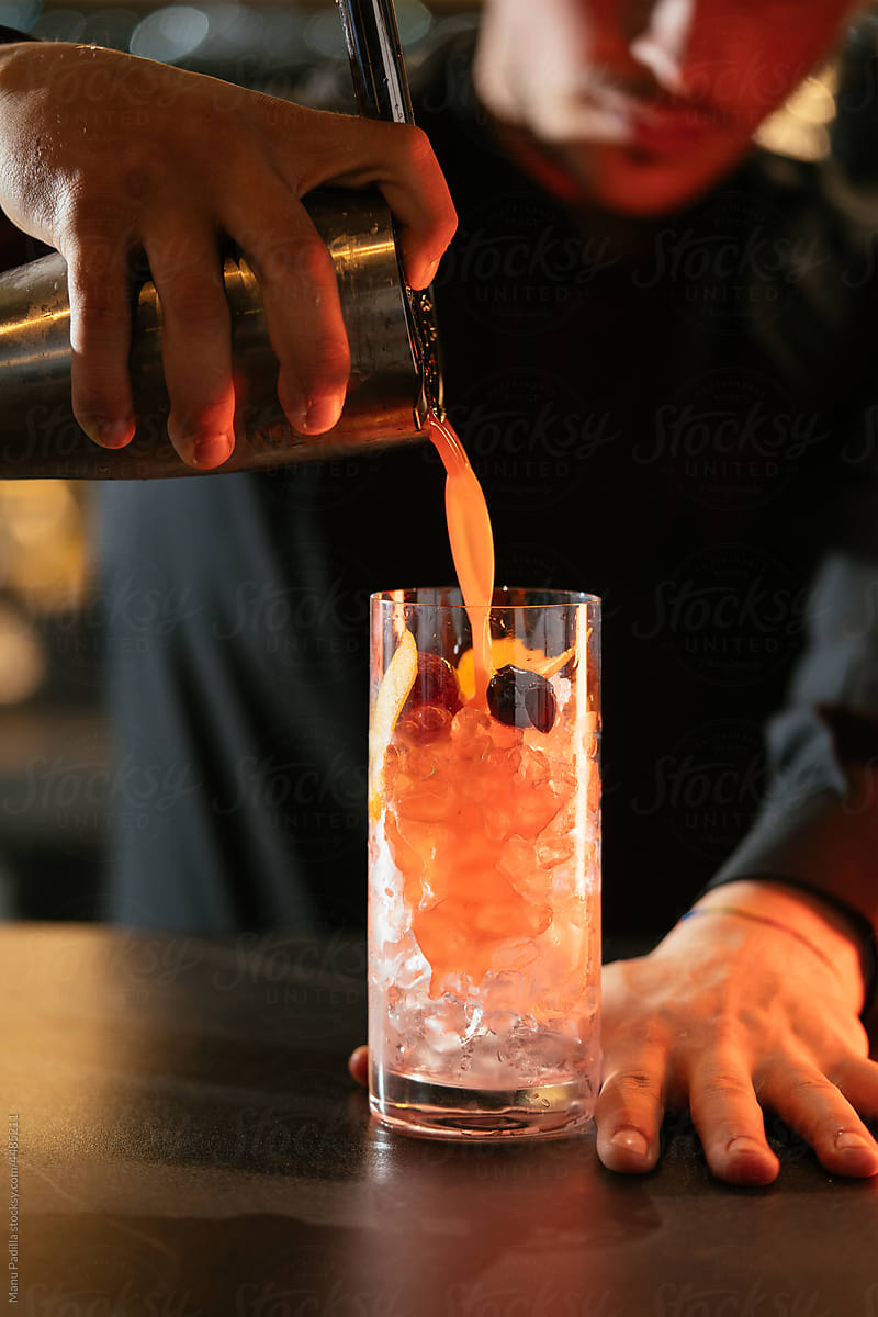 Bartender preparing cocktail in glass with ice cubes