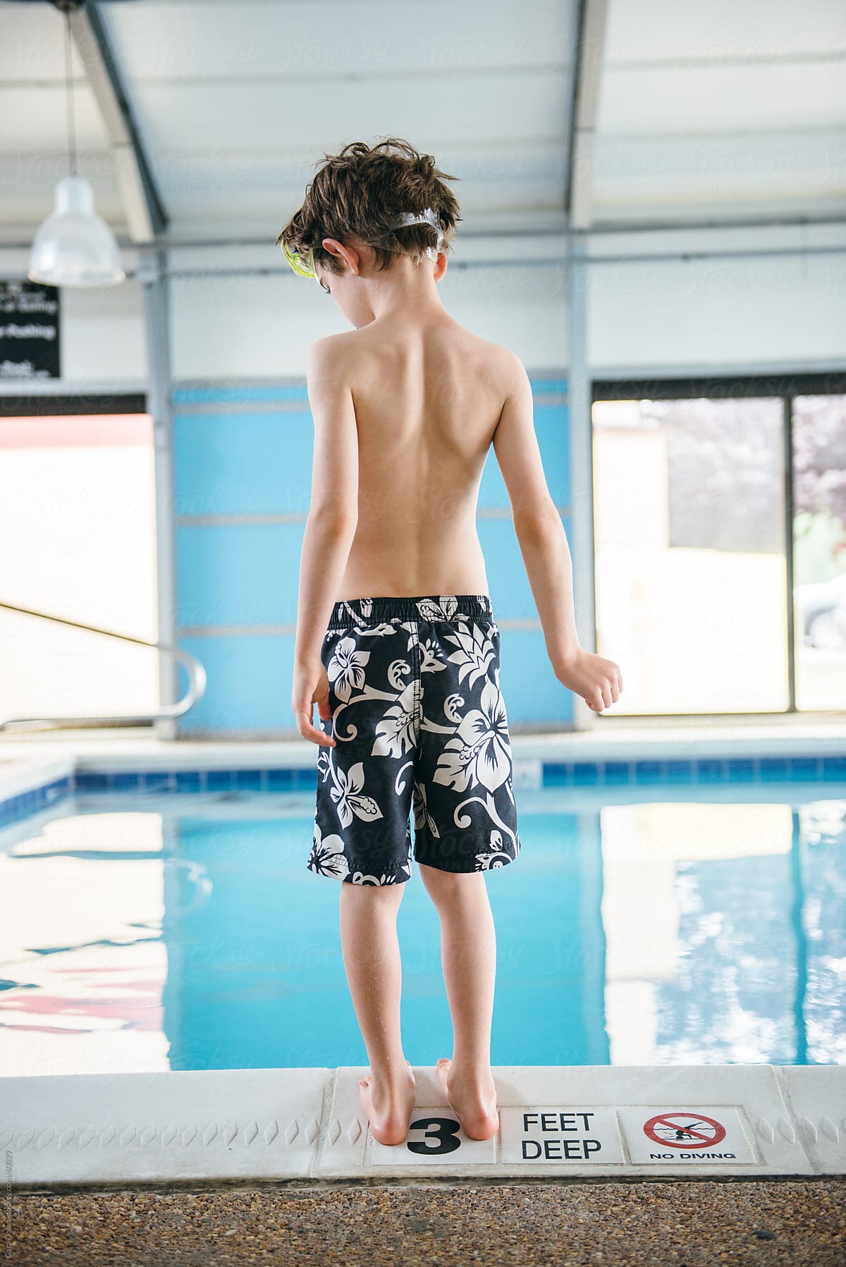 Boy in swimsuit stands at the edge of an indoor swimming pool