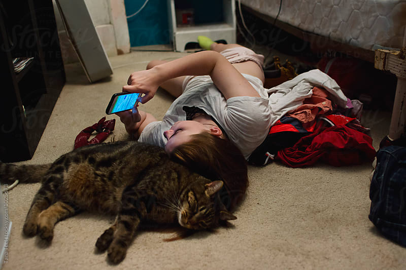 teenager lays on bedroom floor looking at phone