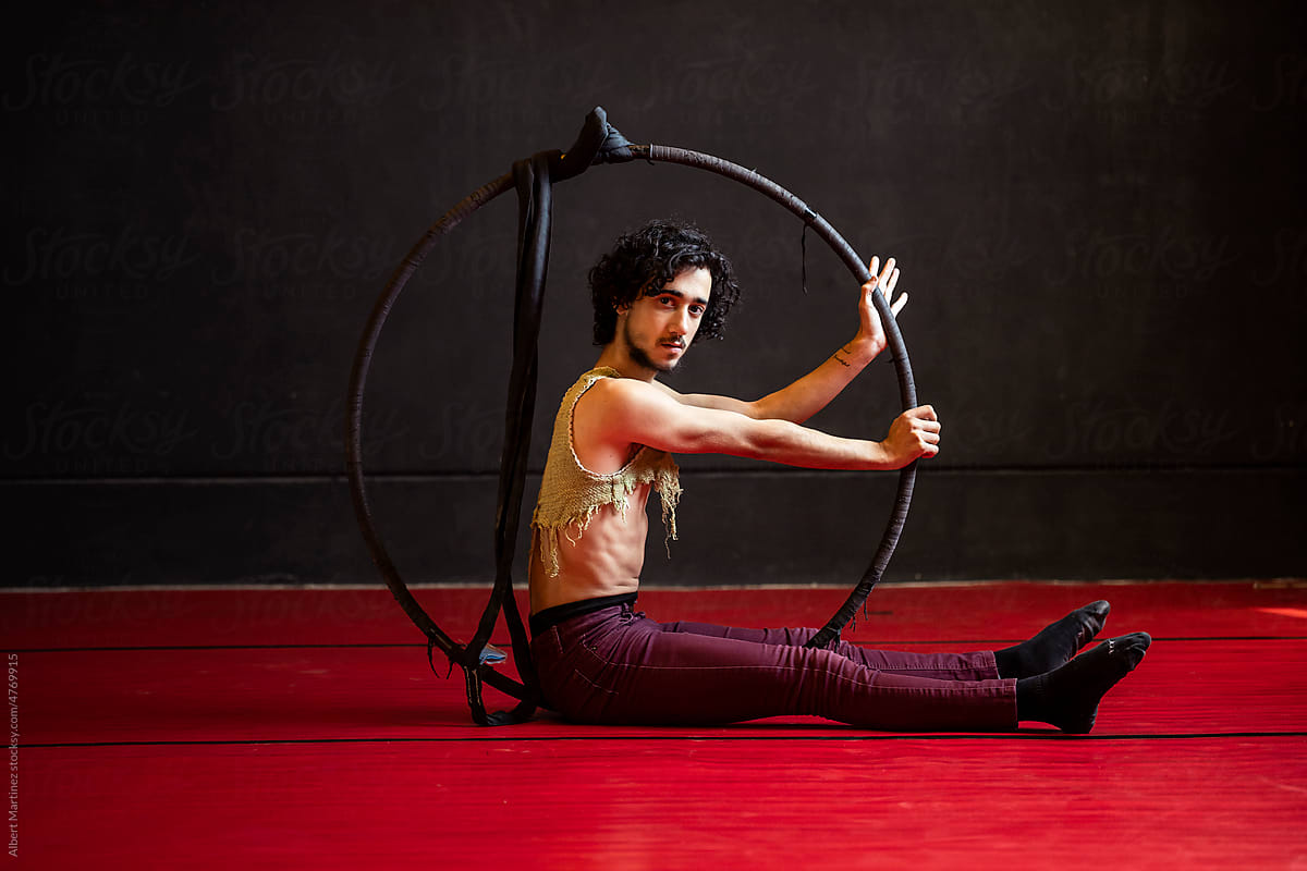 Young male circus performer with hoop lying on floor