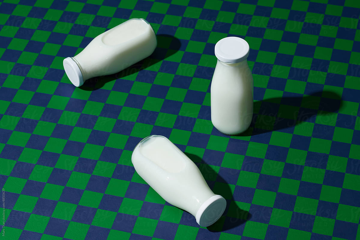 Bottles of organic milk on checkered table against green background.