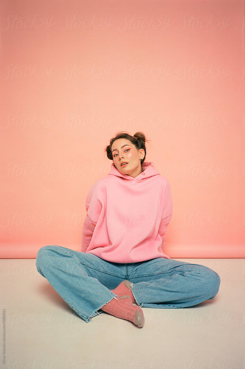 Young woman sitting on floor in studio on peachy pink background