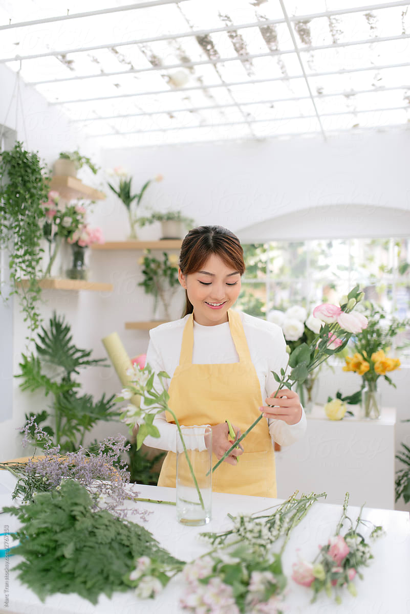 Asian florist standing at table in her flower workshop