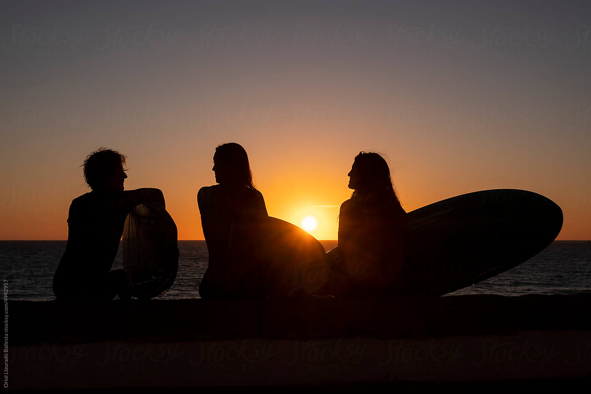 Three surfer girls looking at a sunset