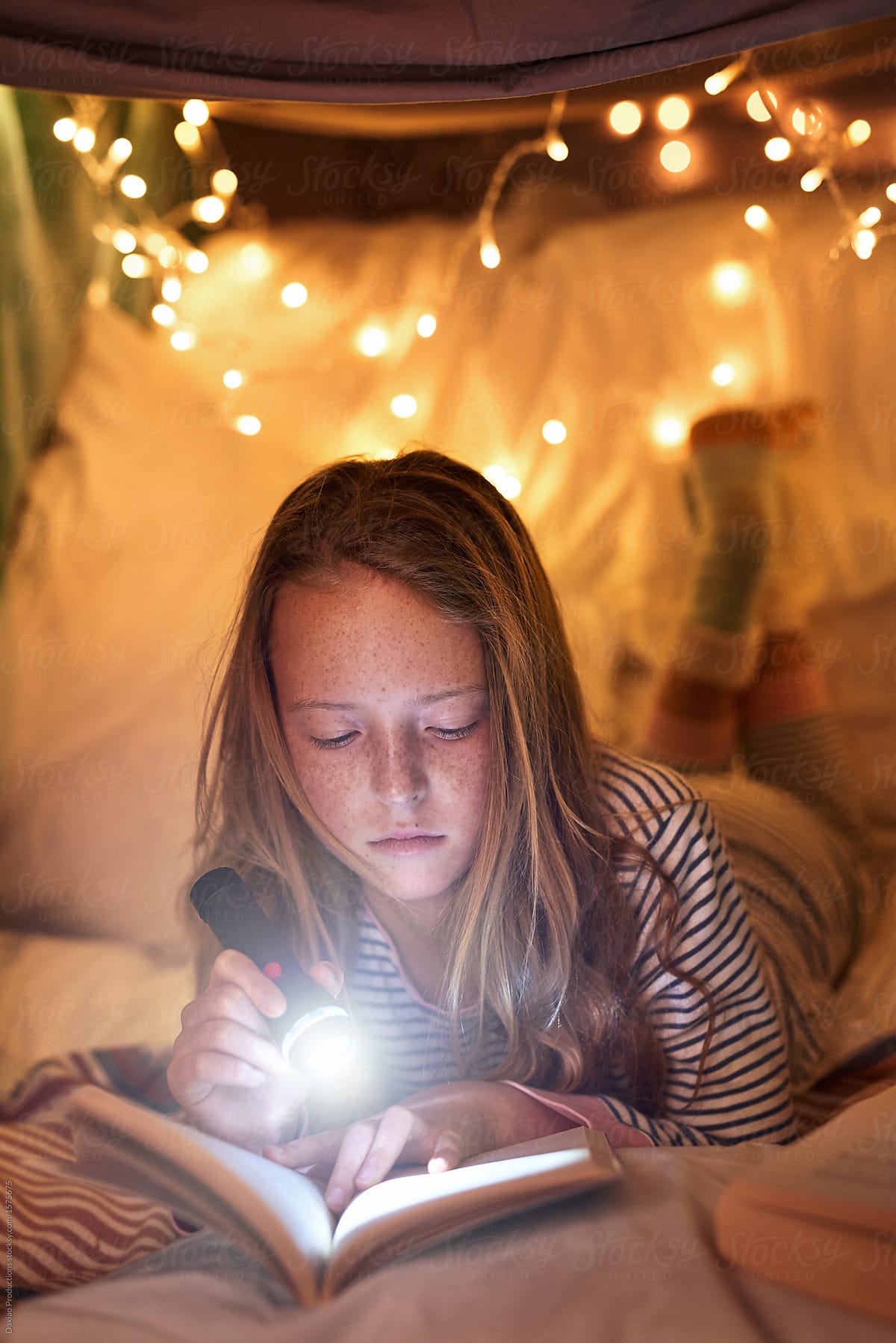 Young girl reading in blanket fort