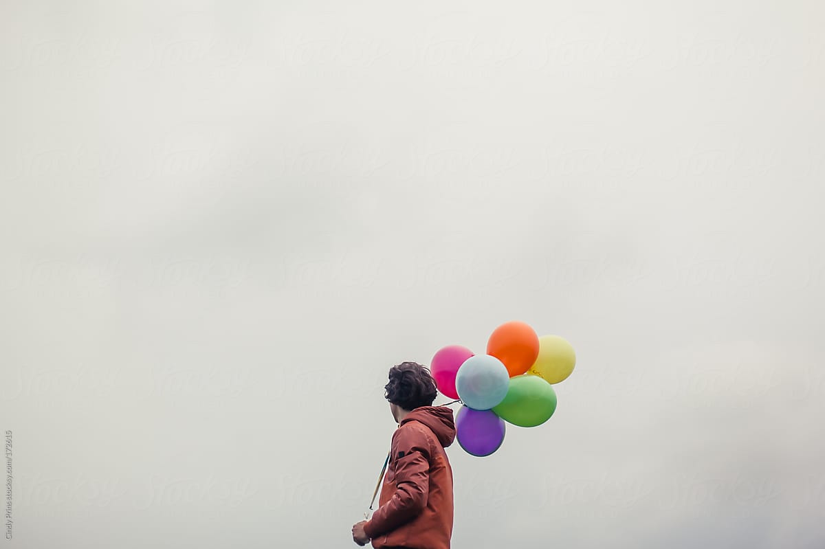 Teenage boy against a cloudy sky holding a bunch of balloons