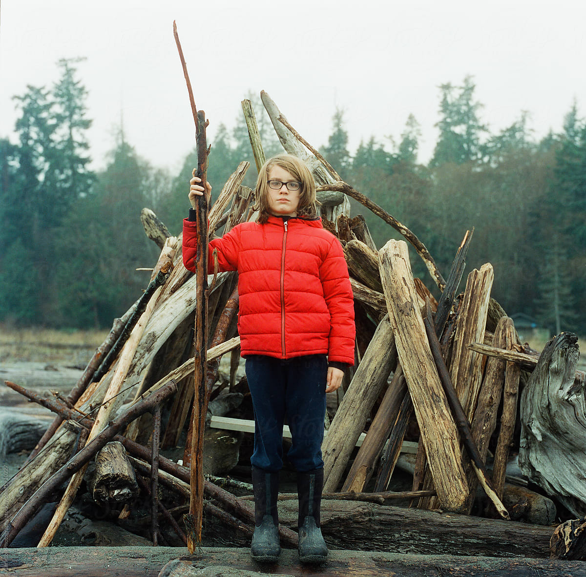 Boy stands guard with stick in front of driftwood castle
