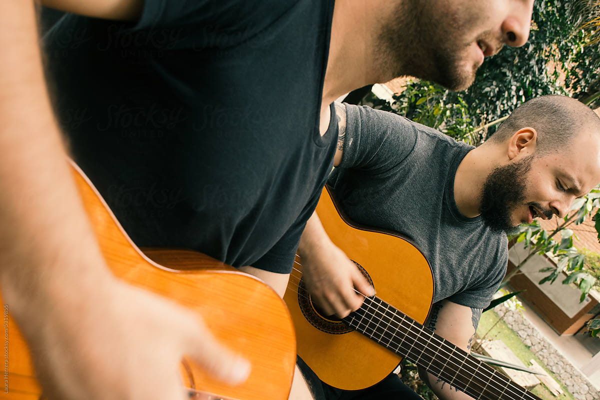 Two men playing guitars on a park bench