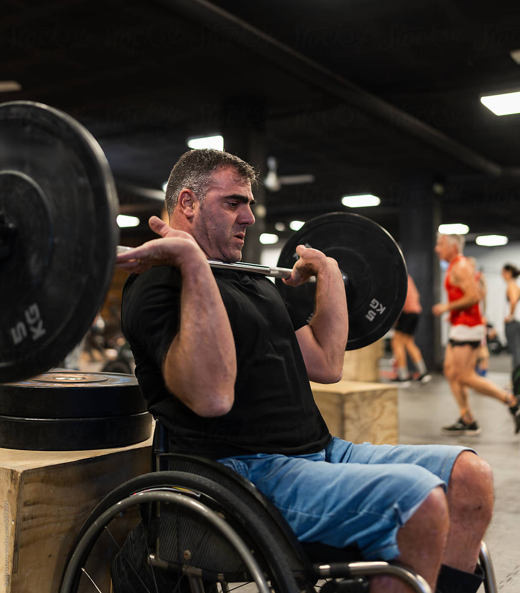 Man in wheelchair lifting a barbell with weights at the gym