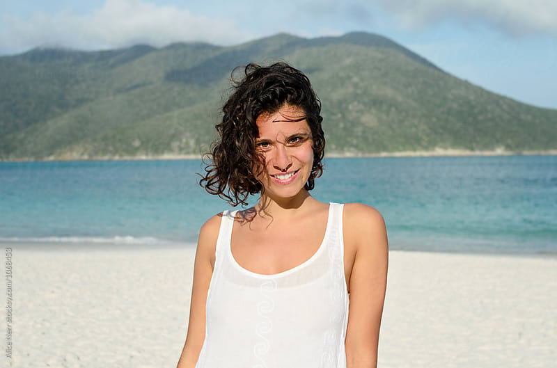 Young woman with curly hair and pierced nose in white at the beach on a windy day