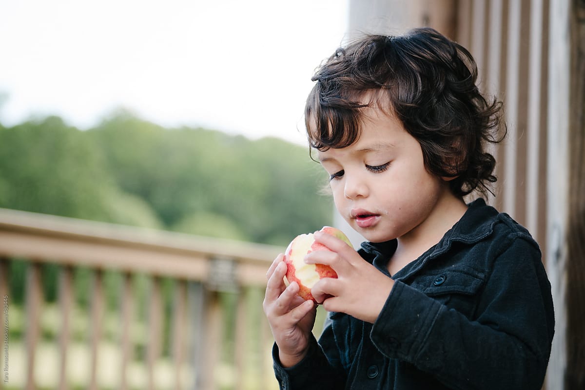 little boy prepares to take another bite out of an apple