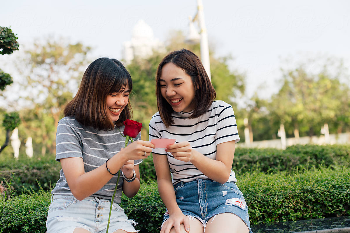 2 Asian girls with red rose in the park reading message on valentine's card
