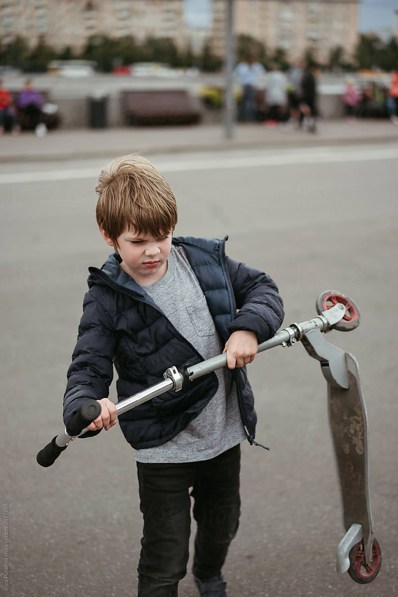 A little boy rides a scooter in the park.