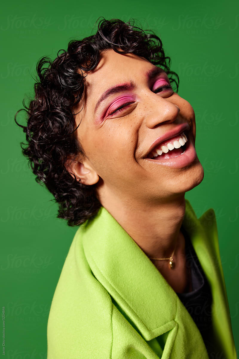 Happy extravagant male laughing against green background