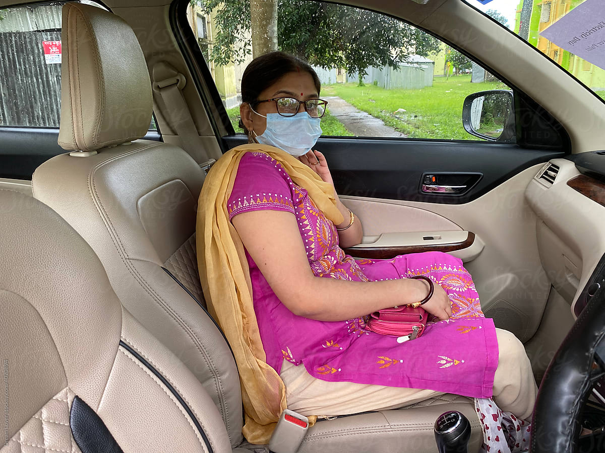 Indian middle aged woman sit inside car wearing mask