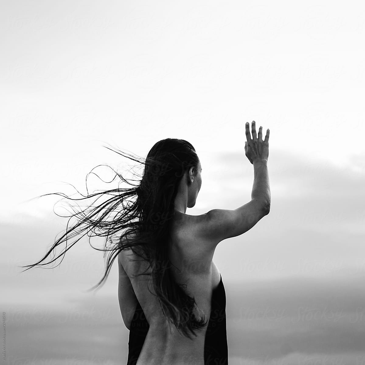 Young naked woman with raised hand at sunset