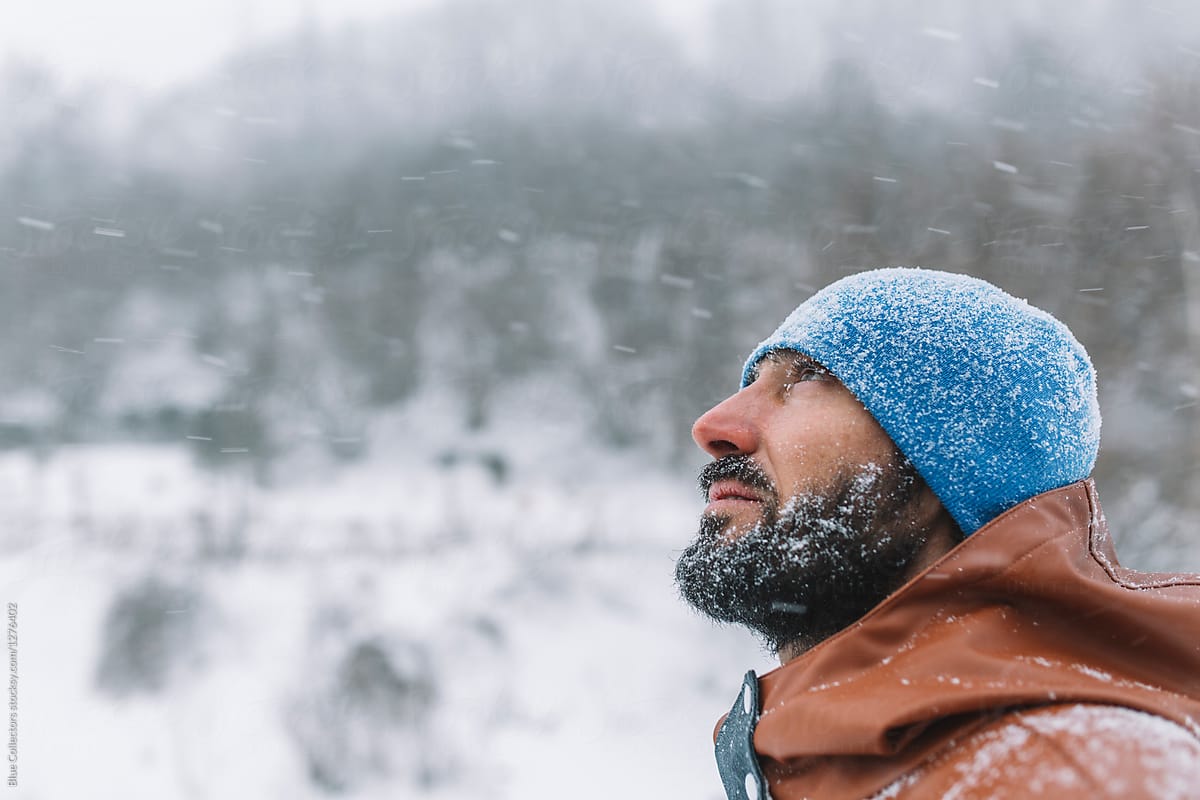 portrait of bearded man covered with snow walking in a snowy road at hard winter day