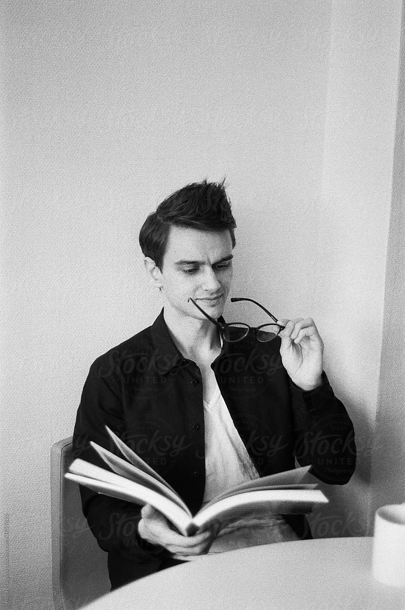 A black and white film portrait of a young beautiful man reading a book