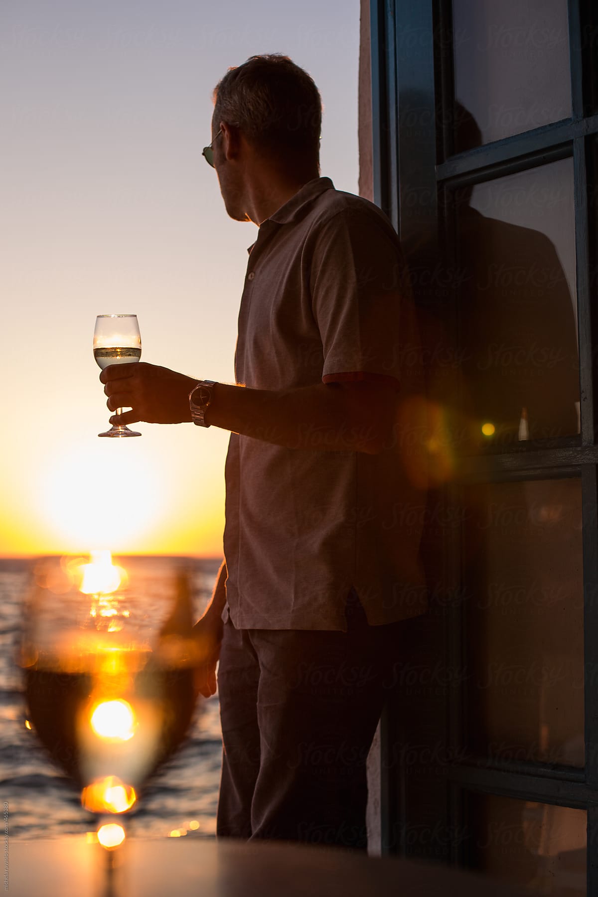 Man looking at the sunset with a glass of white wine in hand