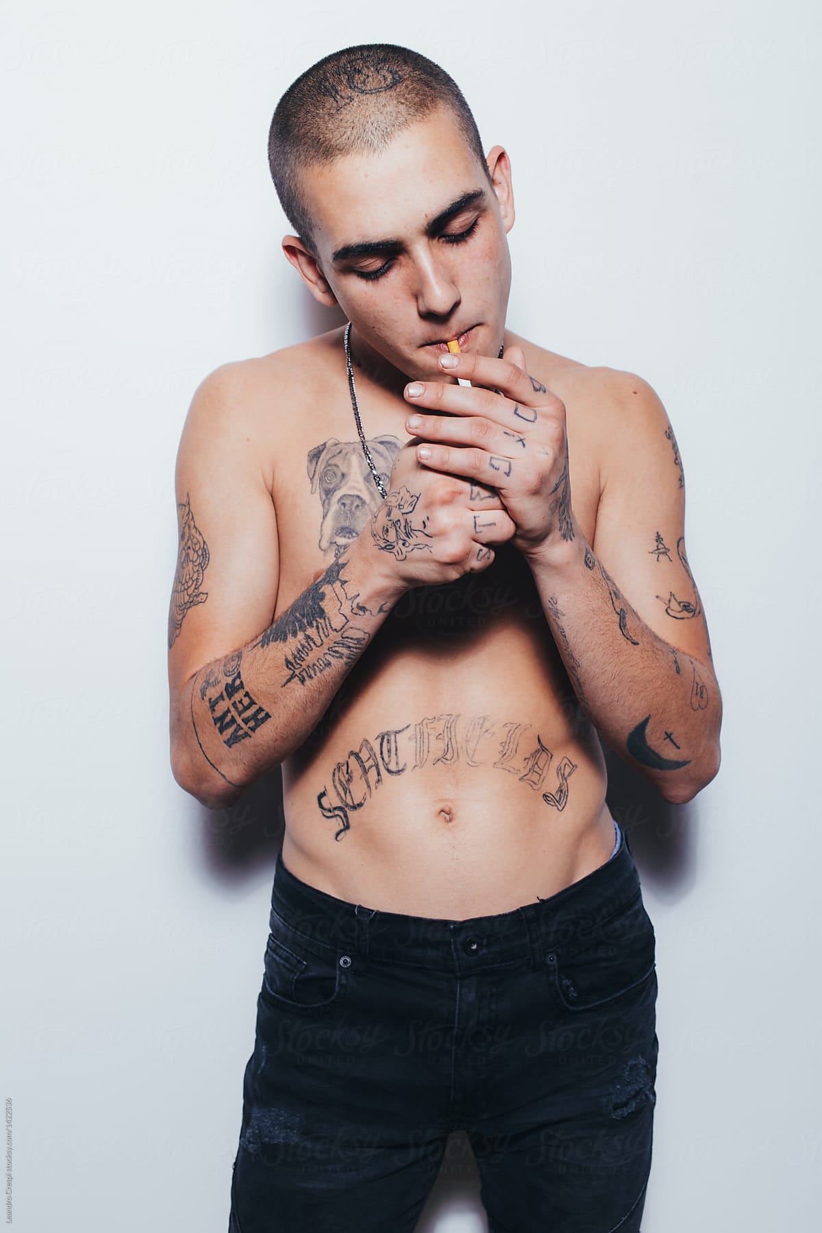 Tattooed young man smokes a cigarette over white wall