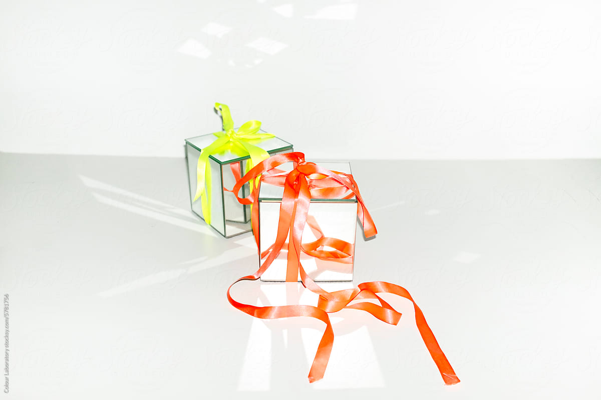 Contemporary photo of shiny mirror presents with neon silk ribbons