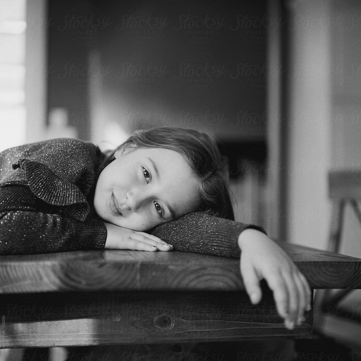 Black And White Portrait Of A Pretty Young Girl Laying On A Kitchen Table By Stocksy 