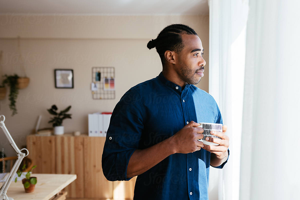 Black man with mug resting near window