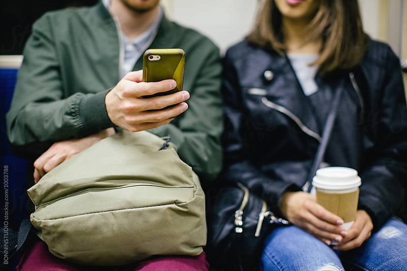Closeup of friends sitting in subway using smartphone.
