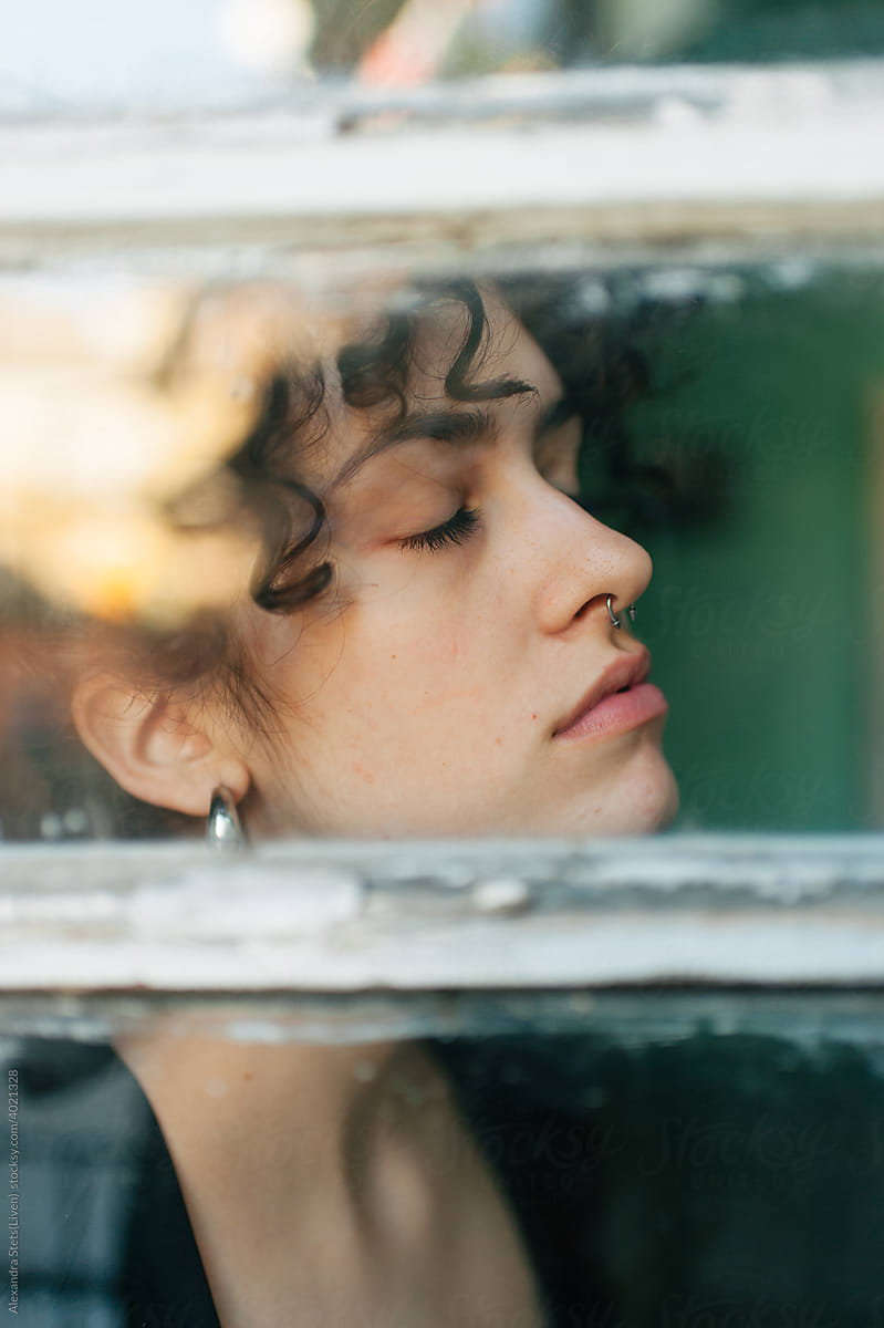 Cute girl with closed eyes through the old balcony glass