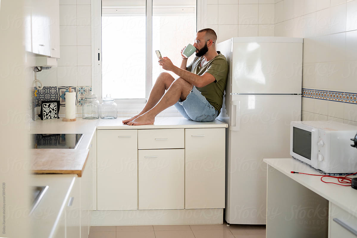 Man drinking coffee and texting at kitchen