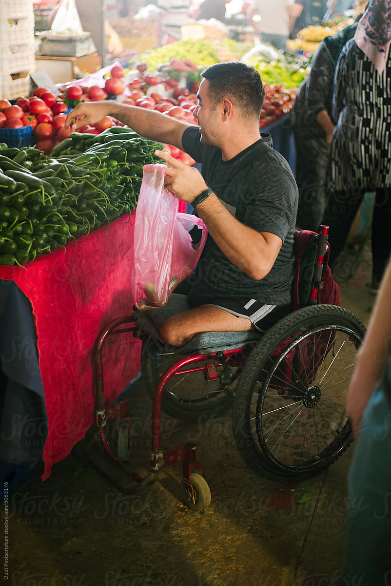 Adult man on a wheelchair chooses fresh cucumbers at a street market