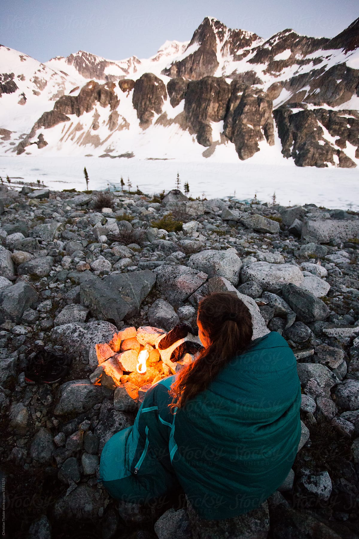 A girl sitting beside a small fire in the mountains