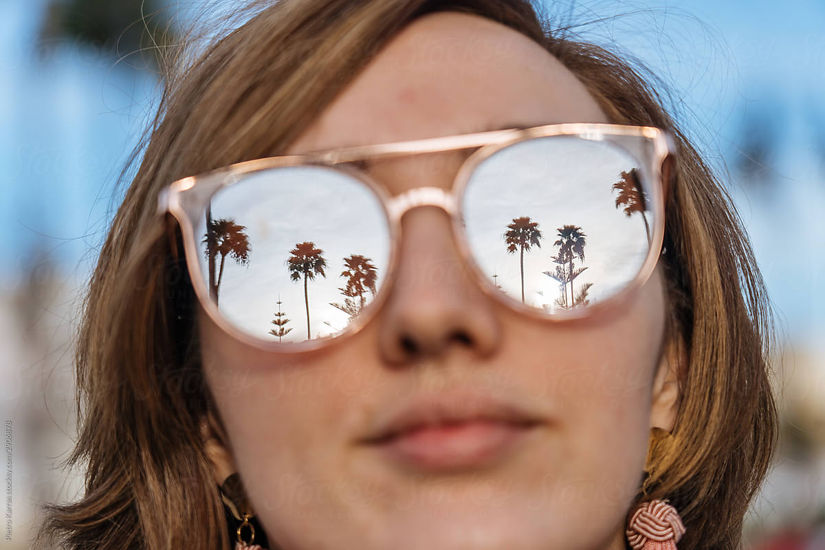 Female face with glasses reflecting sky and palms