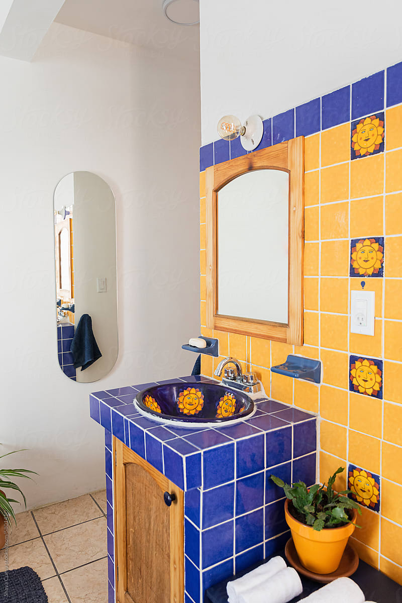 A sink outside a bathroom with a mirror and yellow and blue tiles