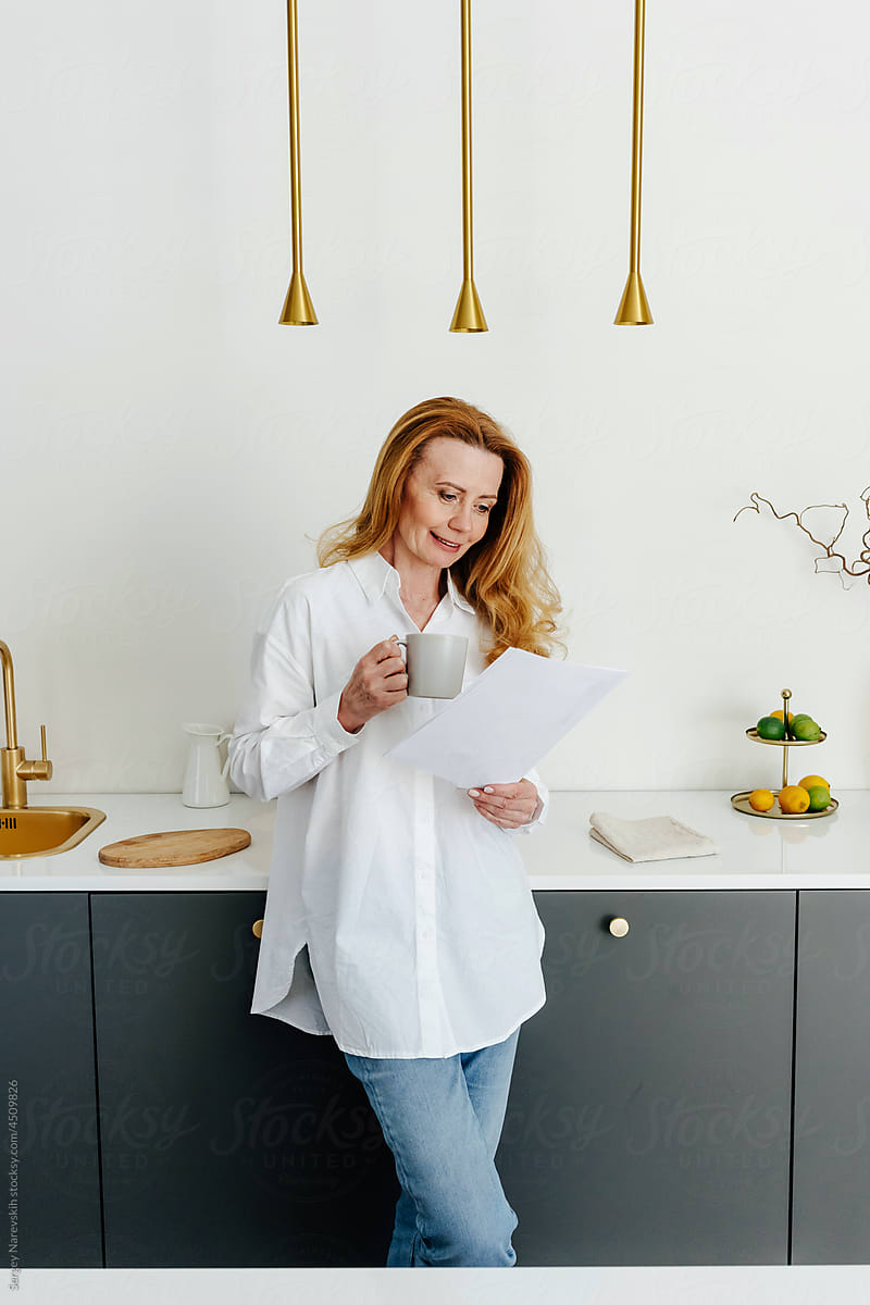 Woman reading document while drinking coffee in kitchen