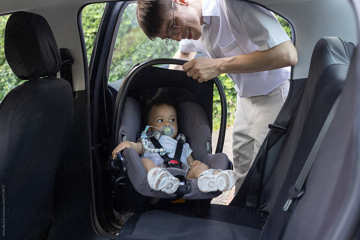 father putting baby in car seat and fasten seat belt