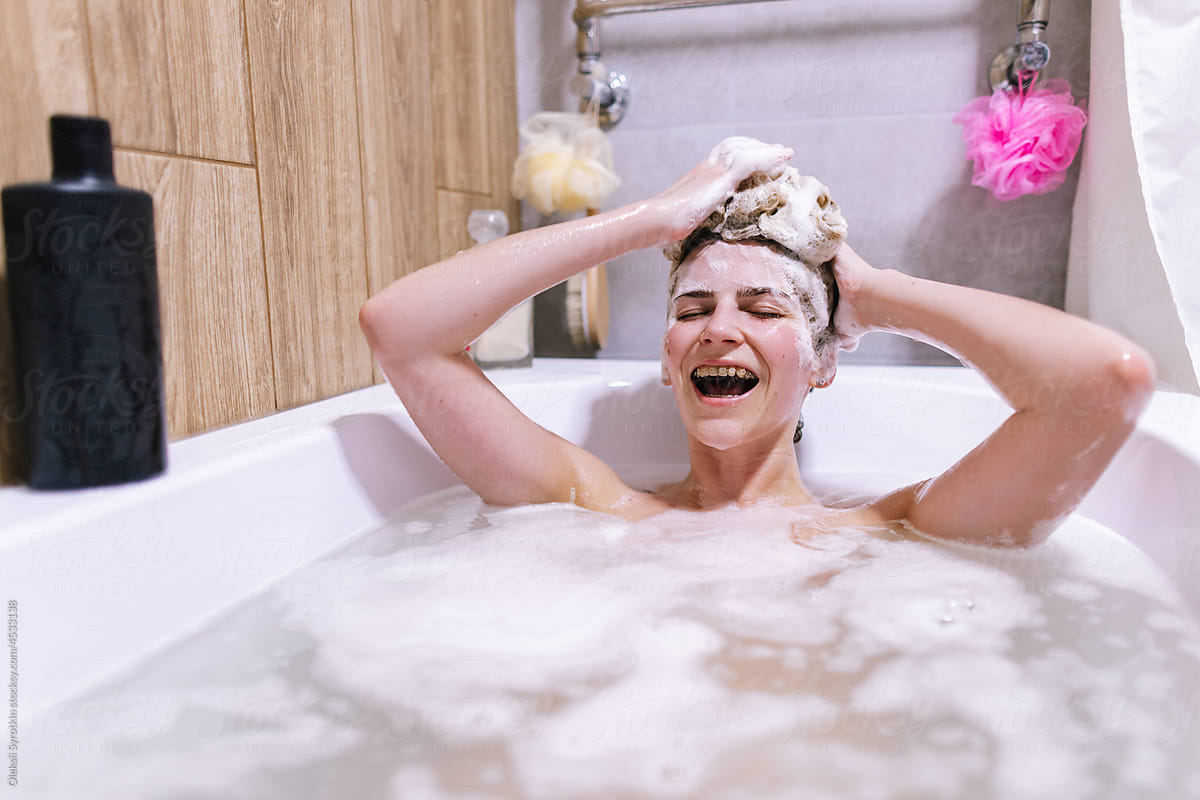 Happy naked woman with lather on head  resting in bathtub