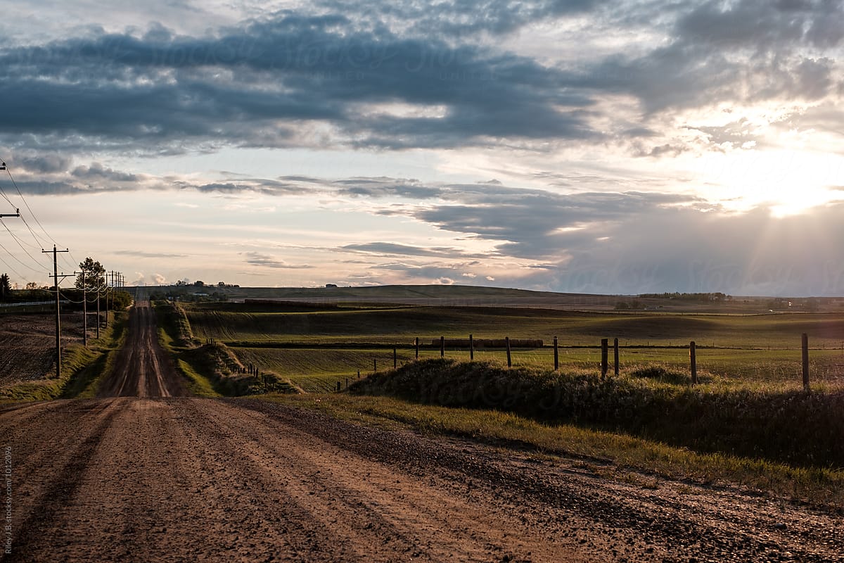 Sun setting over a rural dirt road and farmer's field.
