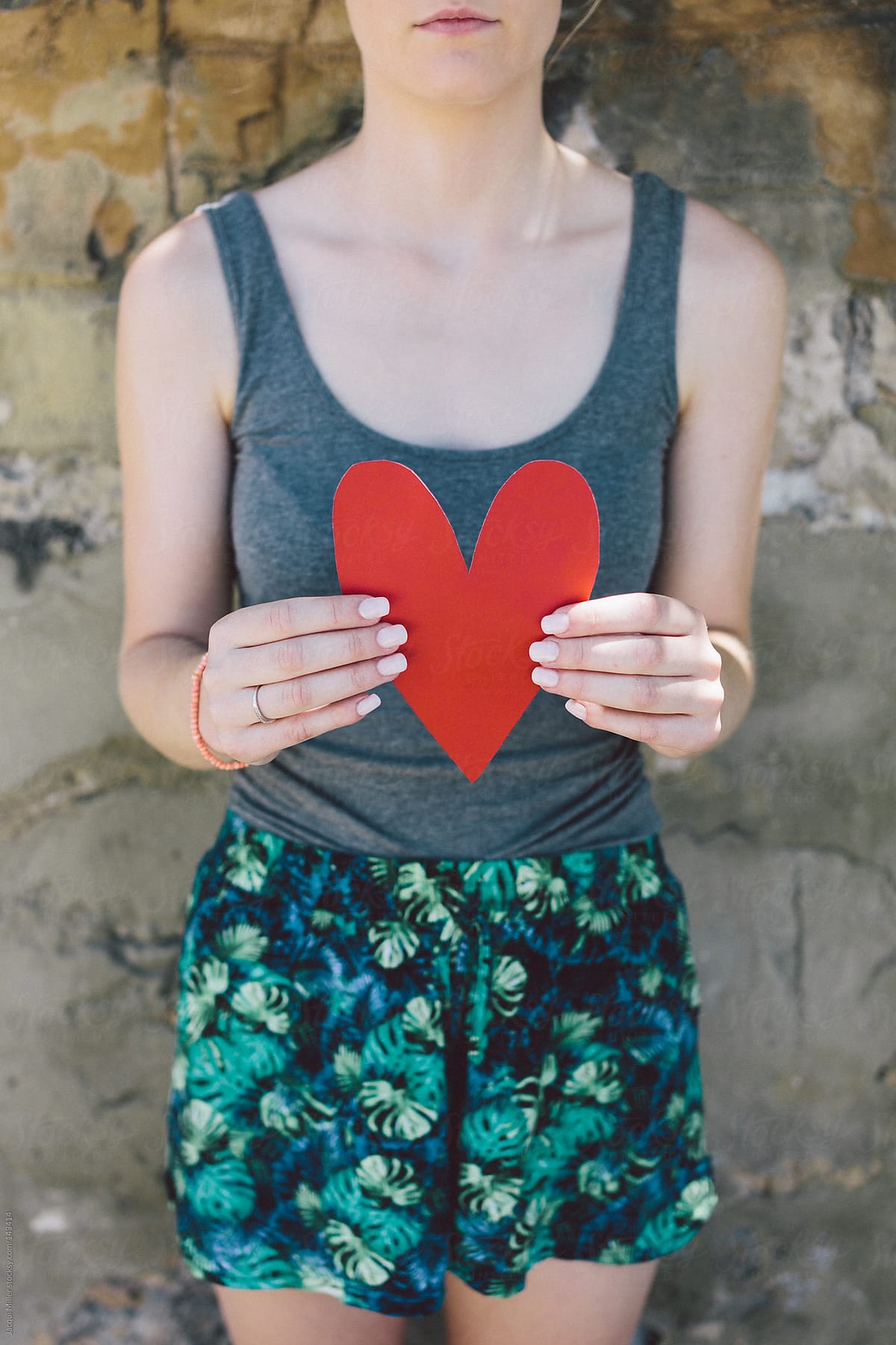 Teenage girl holds a red paper heart in front of her body