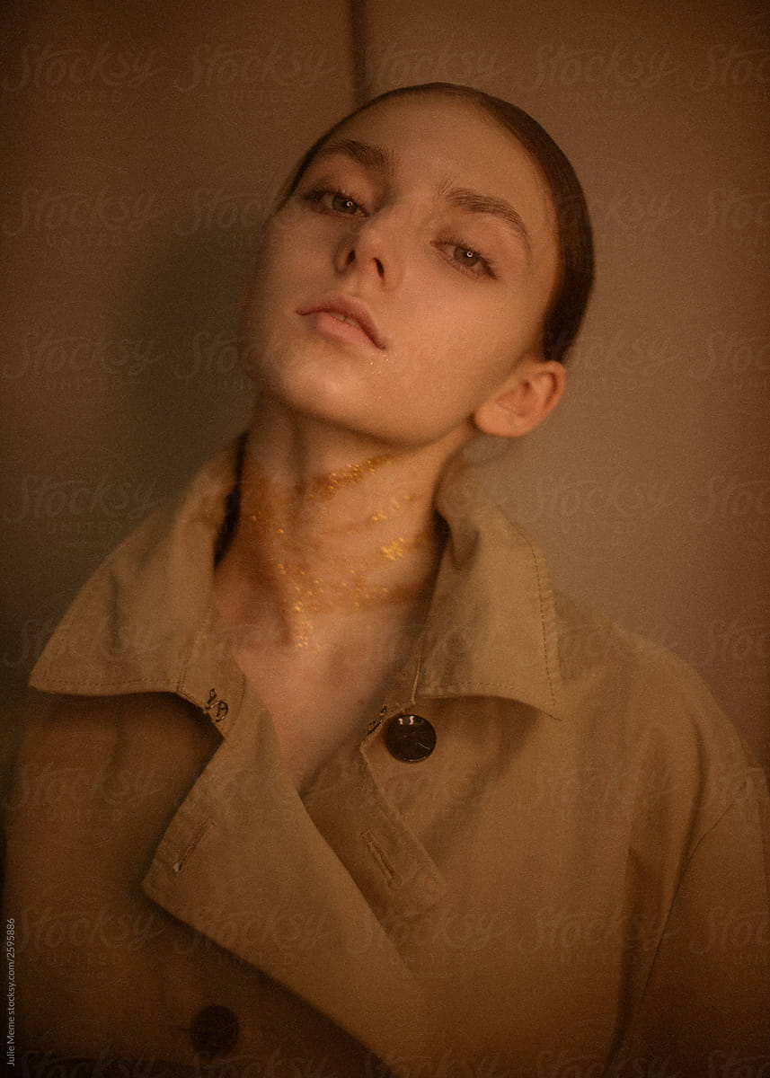 Portrait of a girl with golden hand print on her neck in a coat who stares at you