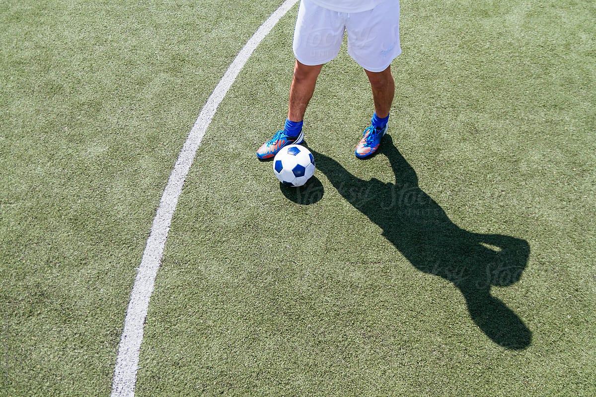 View of the legs of a soccer player and soccer ball in the field casting a shadow