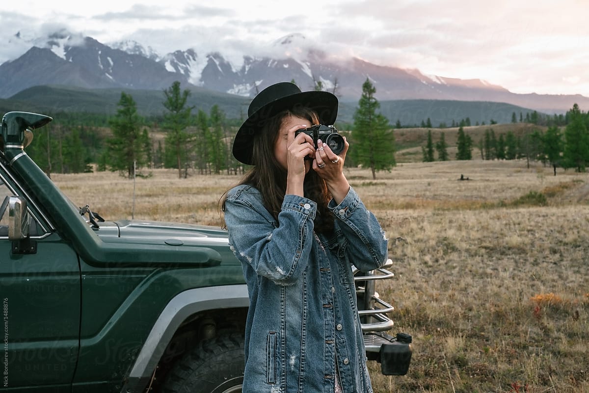 Anonymous young woman taking pictures near old green jeep in wild area