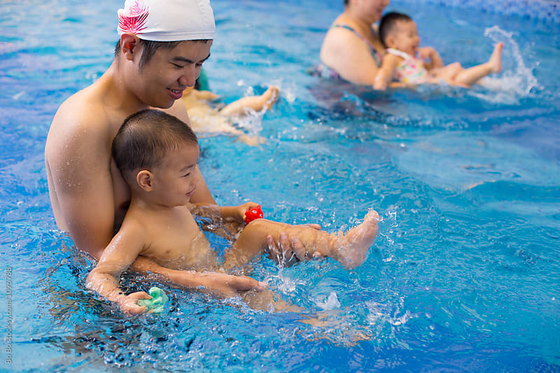 young man teach his baby boy swimming in swimming pool indoor