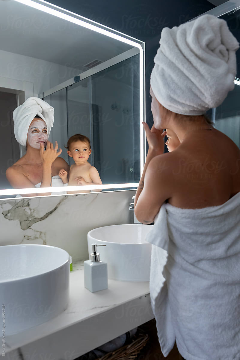 Mother holding child and applying facial mask in bathroom