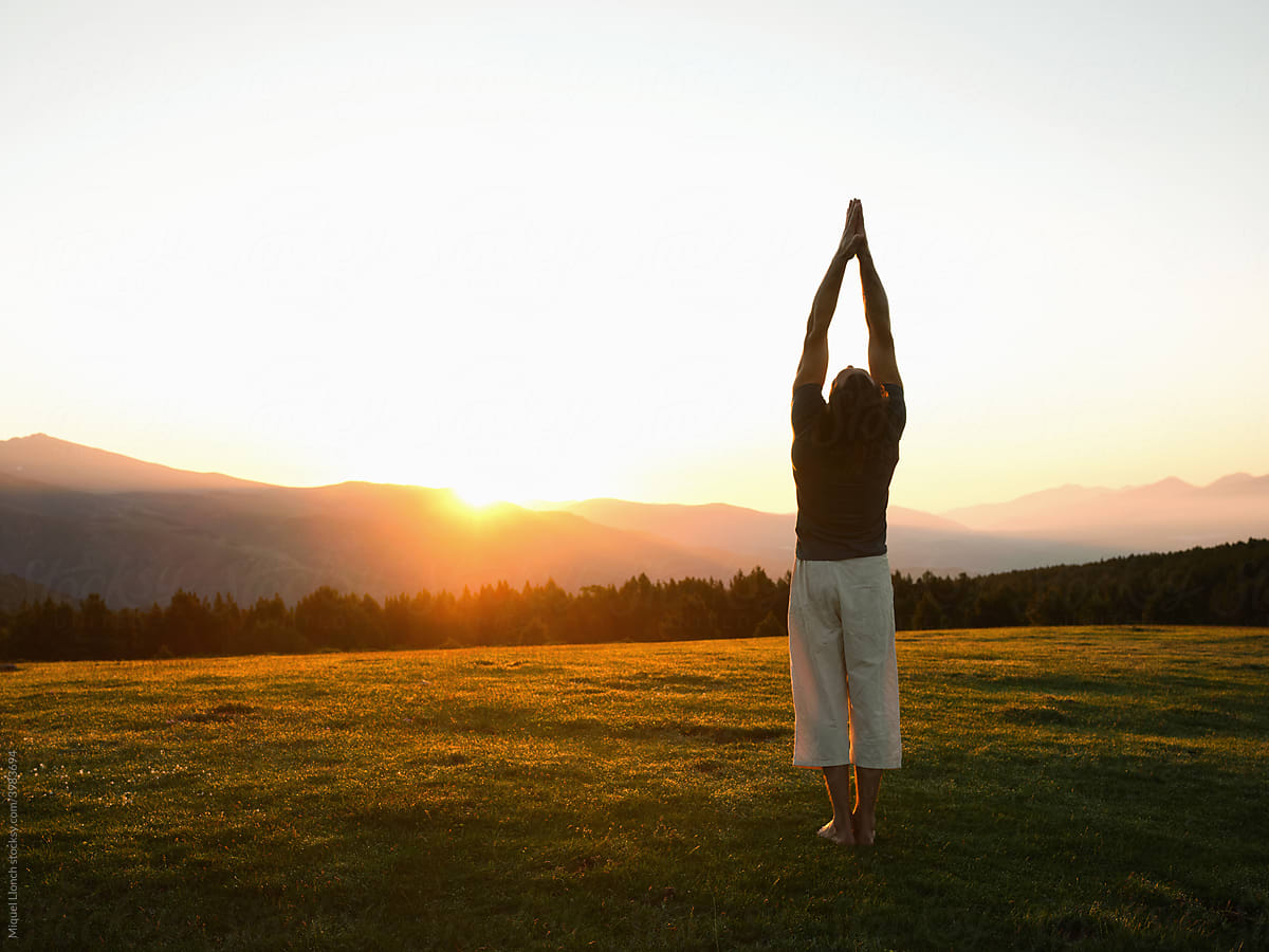 Calm man practicing yoga on field in mountains