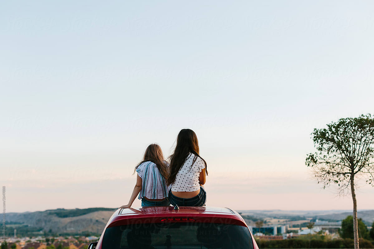 Two young girls looking at horizon on top of a red car