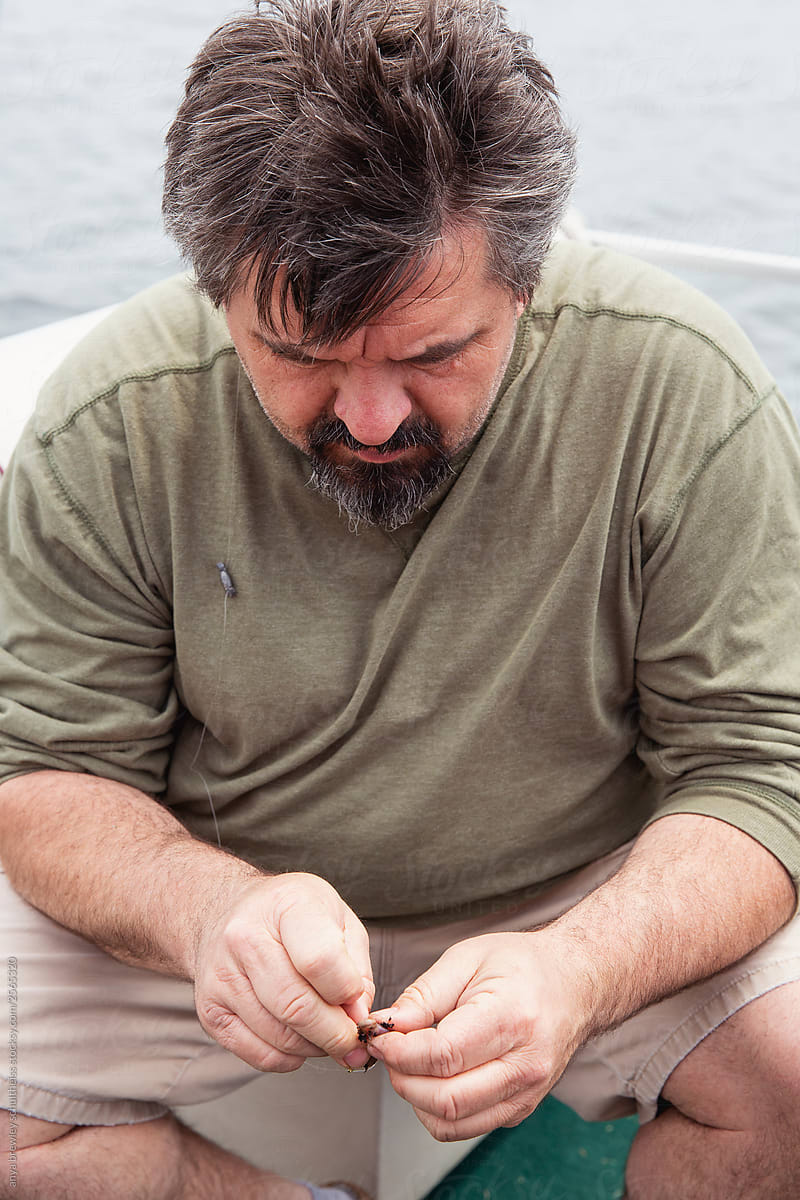 Older man with peppered hair and goatee baiting a hook.
